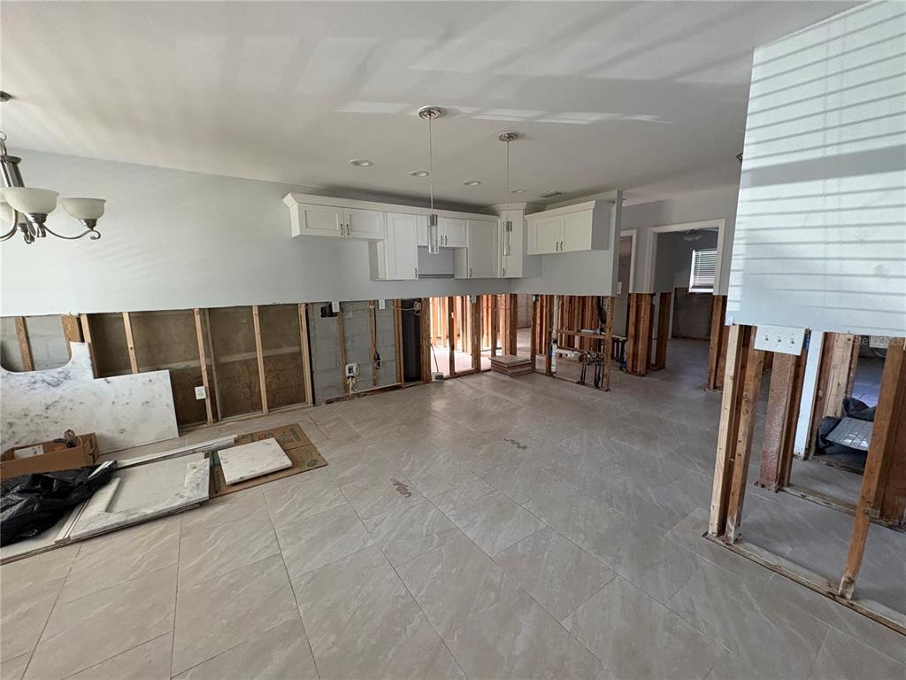 An unfinished kitchen renovation features exposed wall studs, white upper cabinets, and large floor tiles — 6711 S FAUL STREET, TAMPA, FL