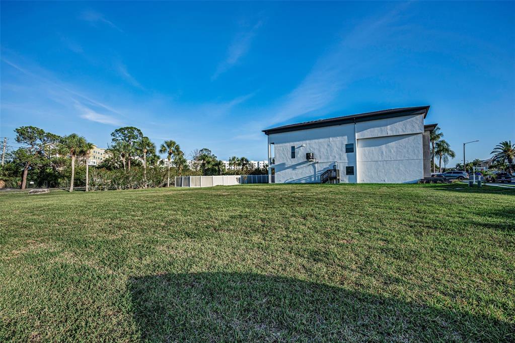 A large, grassy lot sits in front of a white multi-story building under a blue sky — Lot 59 JOBETH DRIVE, NEW PORT RICHEY, FL
