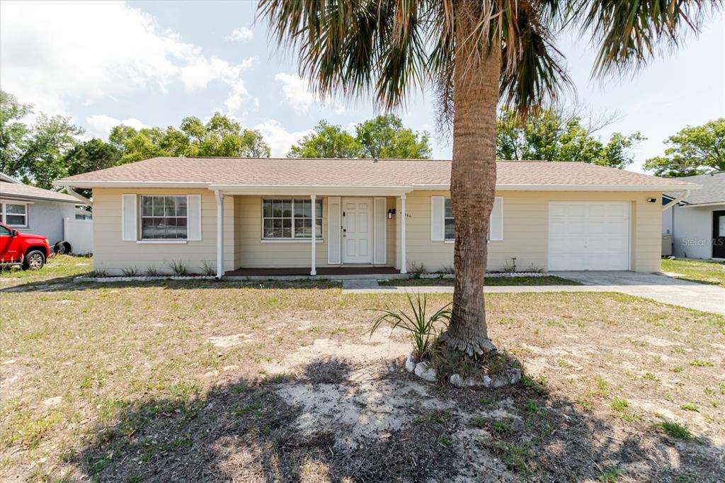 A single-story house with light yellow siding, a front porch, and a palm tree — 12526 ELGIN BOULEVARD, SPRING HILL, FL