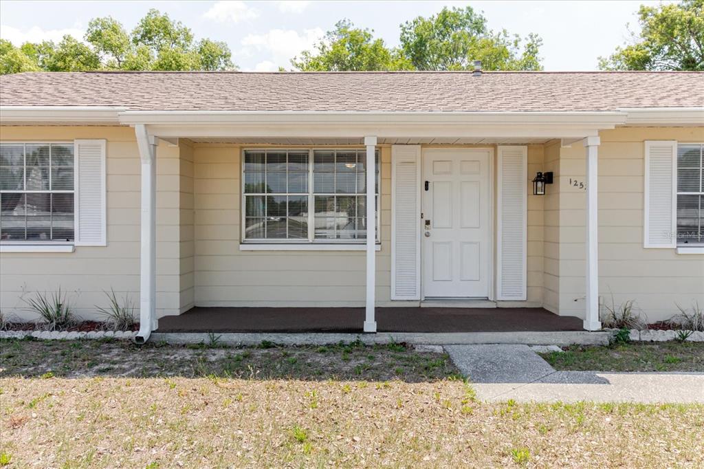 The exterior of a single-story house features beige siding, a covered porch, and white shutters — 12526 ELGIN BOULEVARD, SPRING HILL, FL