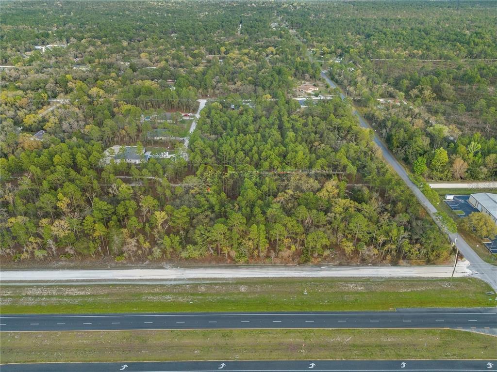 An aerial view shows a wooded lot situated between a highway and a residential area — NICASIO JAY AVENUE, WEEKI WACHEE, FL