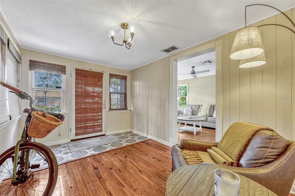 A sunroom with wood floors, a bicycle, a leather chair, and a view into a living room — 2020 PALMER STREET, ORLANDO, FL
