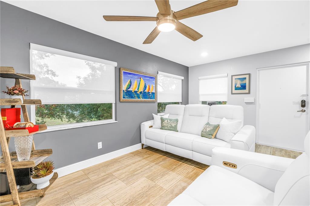 A living room features a white sofa, gray accent wall, ceiling fan, and tile flooring — 224 6TH AVENUE N UNIT 7, ST PETERSBURG, FL