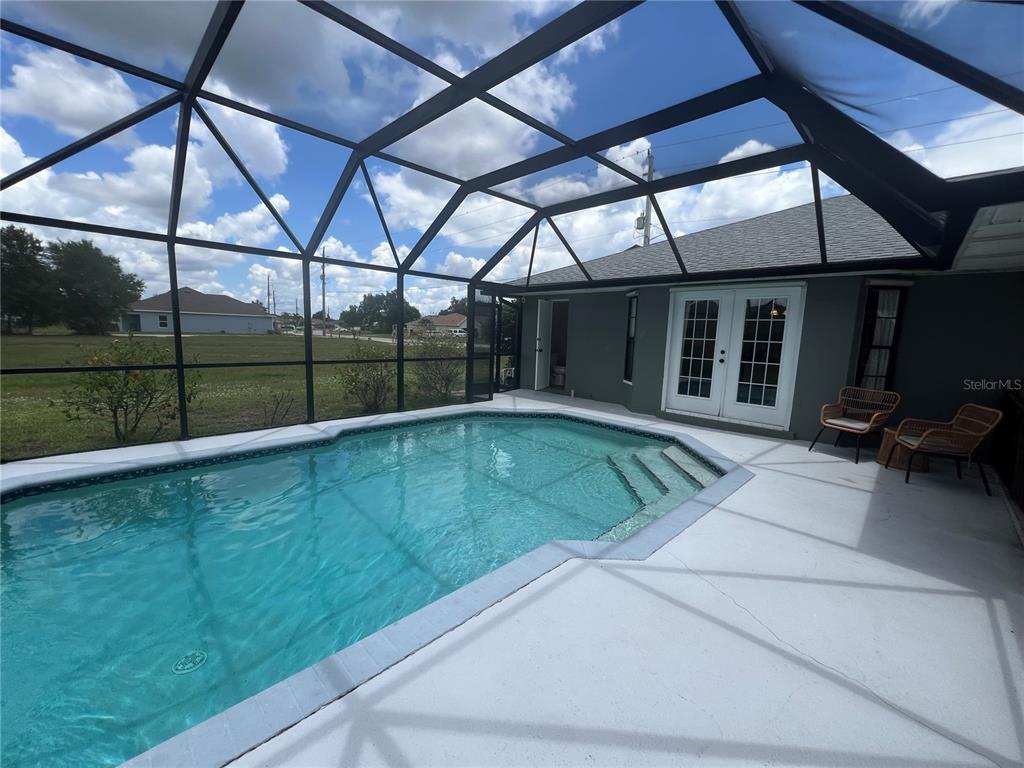 A screened-in pool patio features a concrete deck, a swimming pool, and two wicker chairs — 451 RIO DE JANEIRO AVENUE, PUNTA GORDA, FL