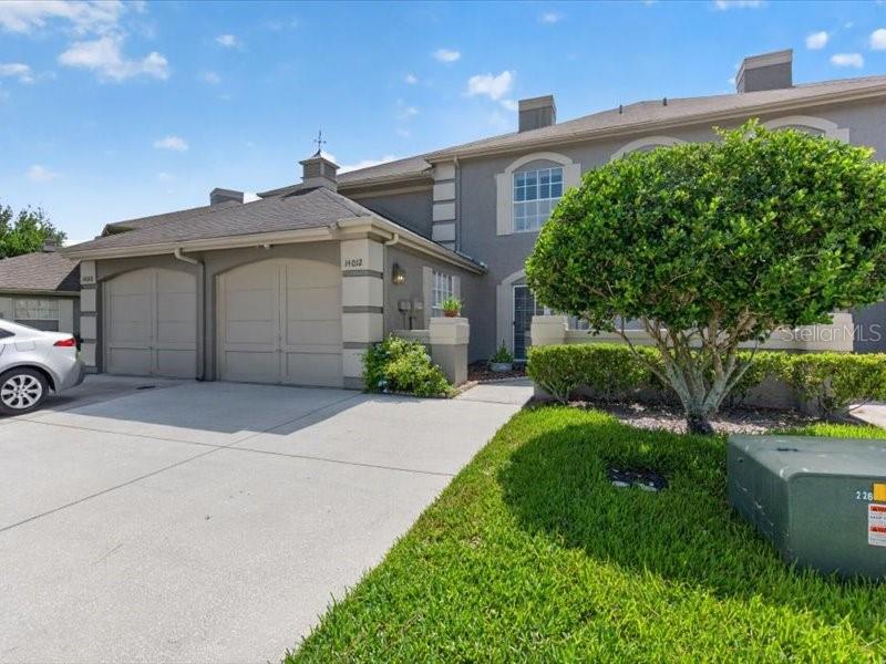 A two-story townhouse exterior features a concrete driveway, a garage, and a small tree — 14012 NOTREVILLE WAY, TAMPA, FL