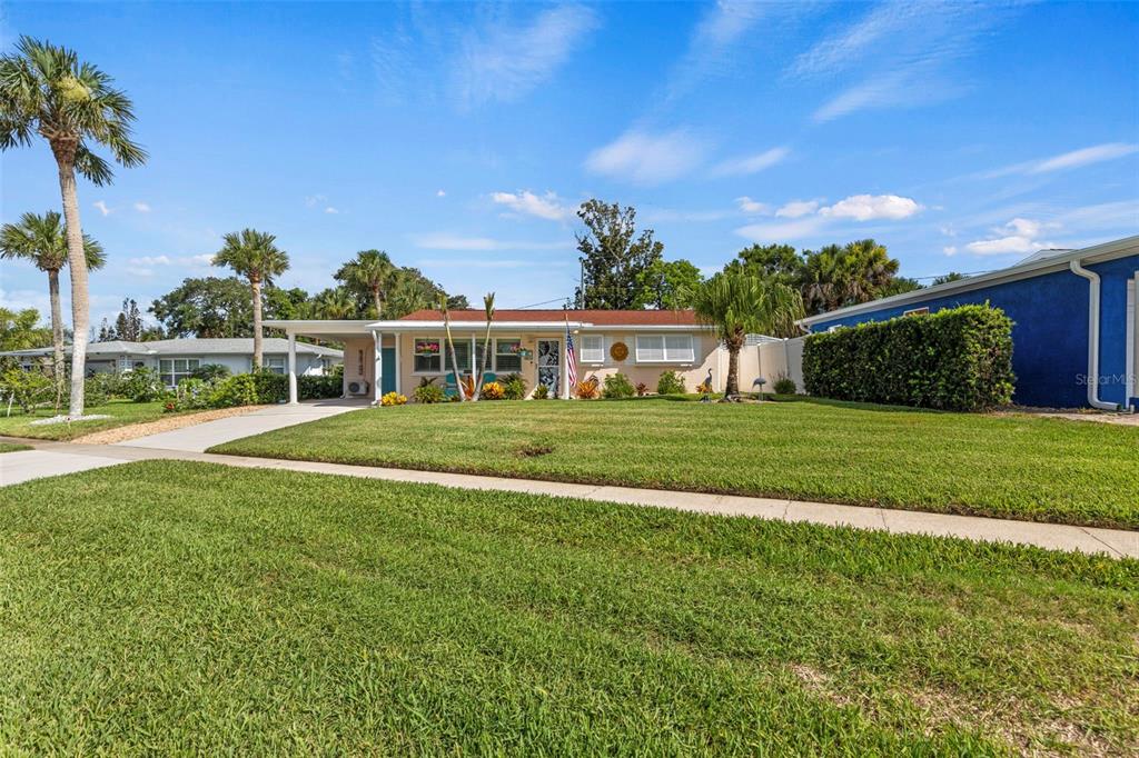A single-story house with a carport and palm trees sits behind a large green lawn — 67 SEABREEZE DRIVE, ORMOND BEACH, FL