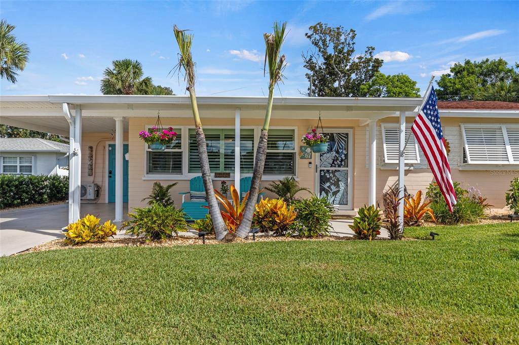 A single-story house with a carport, palm trees, and an American flag in the front yard — 67 SEABREEZE DRIVE, ORMOND BEACH, FL