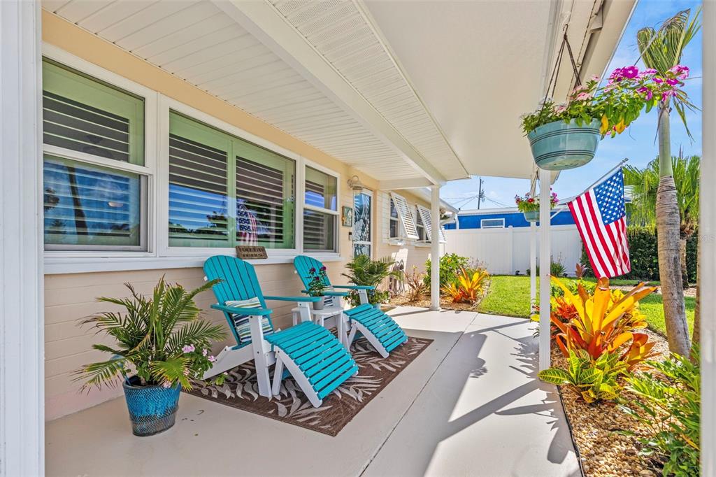 A covered patio features two teal Adirondack chairs with ottomans on a patterned rug — 67 SEABREEZE DRIVE, ORMOND BEACH, FL