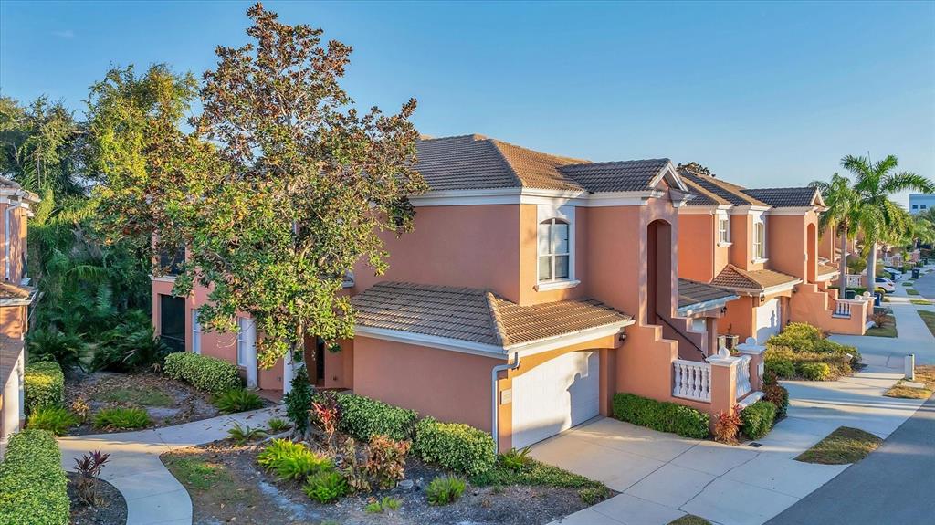 An exterior view of a two-story peach-colored townhouse with a garage and a large tree — 5523 46TH COURT W, BRADENTON, FL