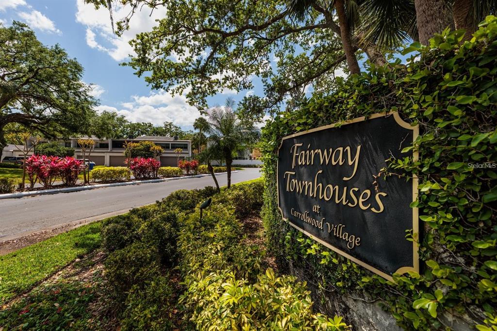 A sign for Fairway Townhouses at Carrollwood Village stands beside a road and landscaped greenery — 4207 FAIRWAY RUN, TAMPA, FL