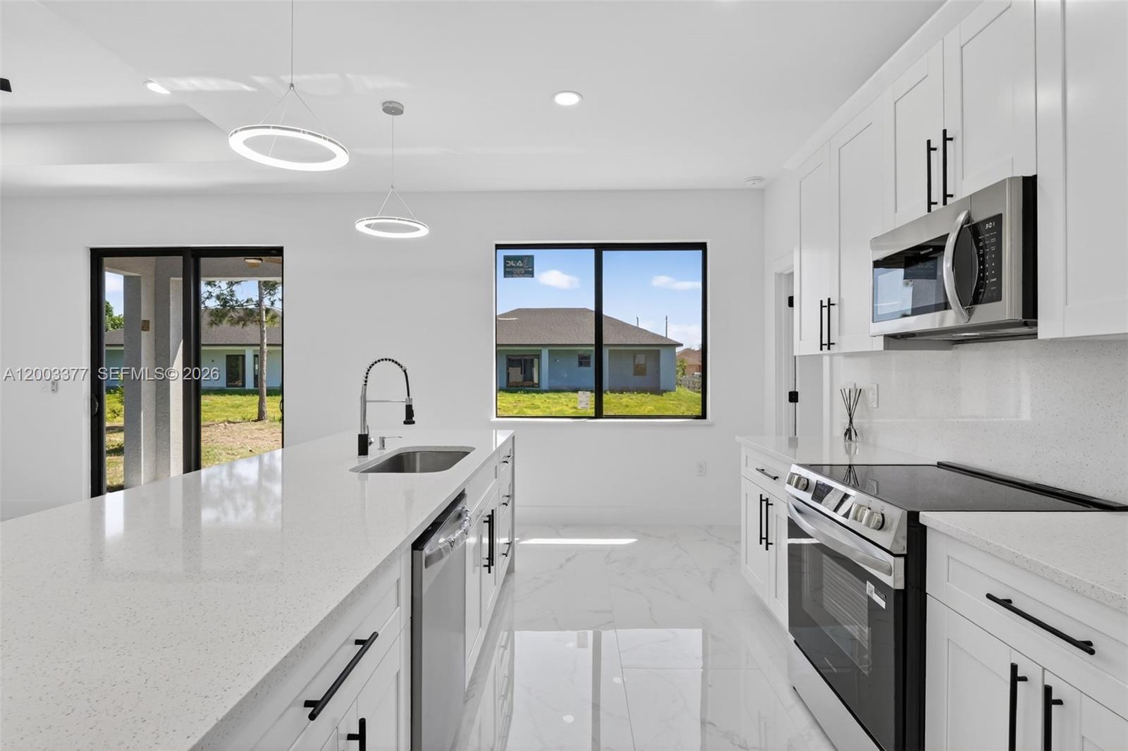 A modern kitchen features white cabinetry, quartz countertops, stainless steel appliances, and tile flooring — 3903 SW 11, Lehigh Acres FL 33976, LEHIGH ACRES, FL