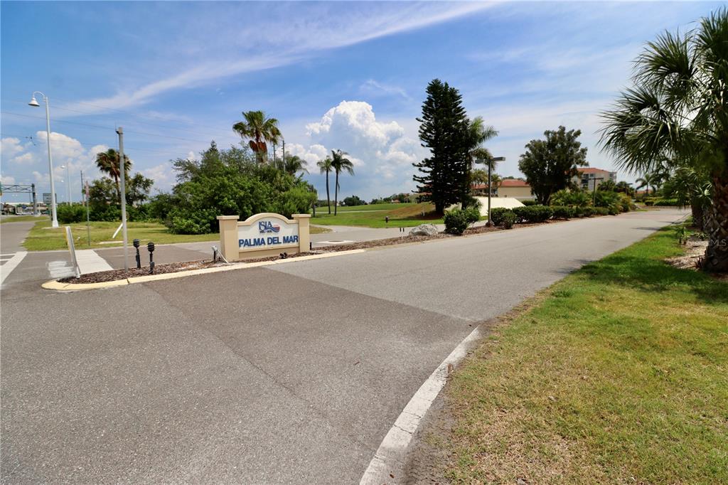 A paved road leads to a sign for Palma del Mar with palm trees nearby — 6219 PALMA DEL MAR BOULEVARD S UNIT 504, ST PETERSBURG, FL