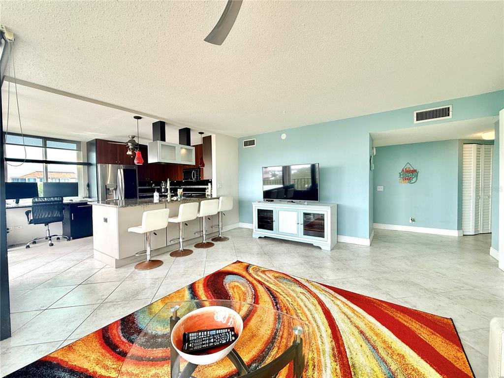 An open-concept living room and kitchen featuring tile floors, a colorful rug, and bar seating — 6219 PALMA DEL MAR BOULEVARD S UNIT 504, ST PETERSBURG, FL