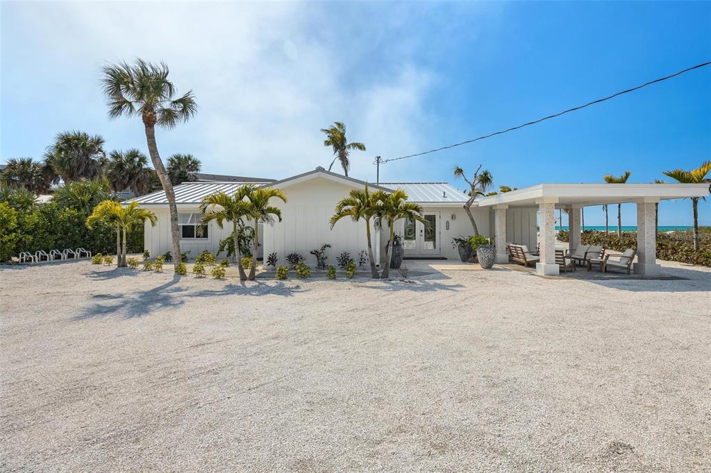 A white house with a metal roof and a covered patio sits on a gravel lot — 2740 N BEACH ROAD UNIT B, ENGLEWOOD, FL