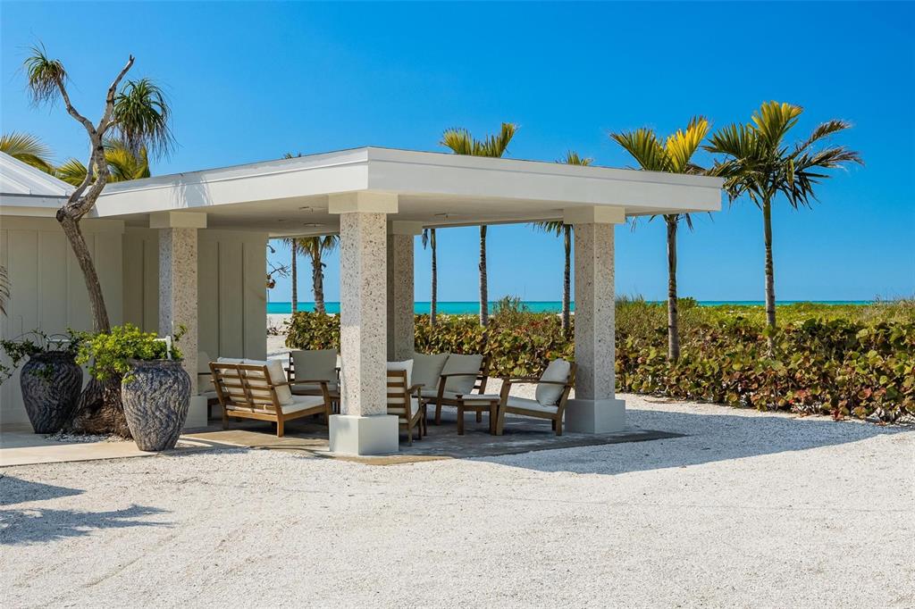 A covered outdoor patio with stone columns and seating overlooks a beach and palm trees — 2740 N BEACH ROAD UNIT B, ENGLEWOOD, FL