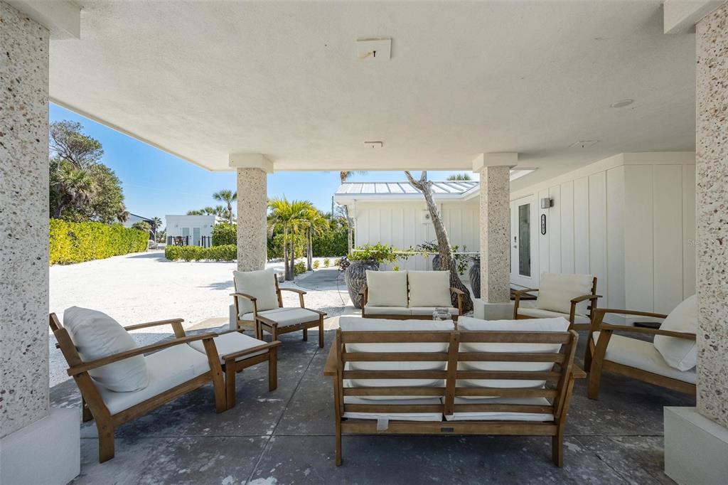 A covered patio features concrete flooring, stone columns, and wooden outdoor furniture with white cushions — 2740 N BEACH ROAD UNIT B, ENGLEWOOD, FL