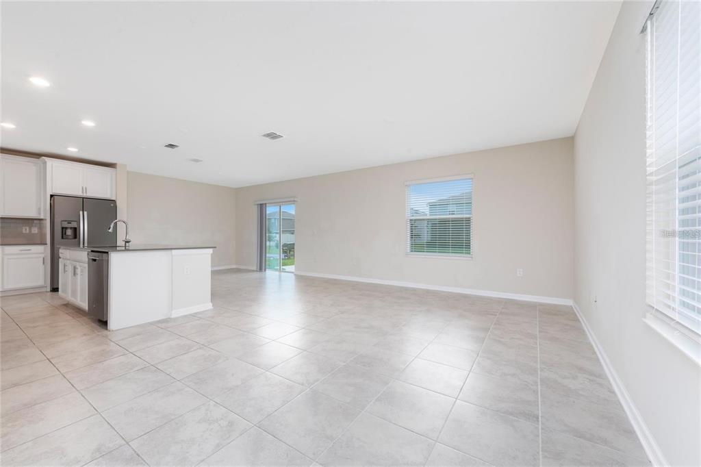 An open-concept kitchen and living area features light tile flooring, white cabinetry, and sliding doors — 2843 ALDER BERRY BOULEVARD, OCOEE, FL