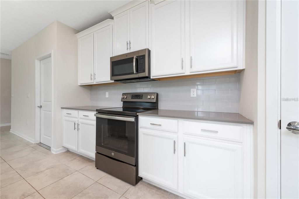 A kitchen features white cabinets, gray countertops, a subway tile backsplash, and stainless steel appliances — 2843 ALDER BERRY BOULEVARD, OCOEE, FL
