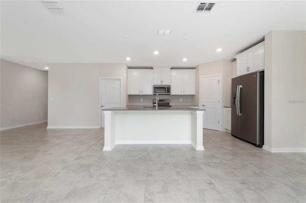 A modern kitchen features white cabinets, a central island, stainless steel appliances, and tile flooring — 2843 ALDER BERRY BOULEVARD, OCOEE, FL