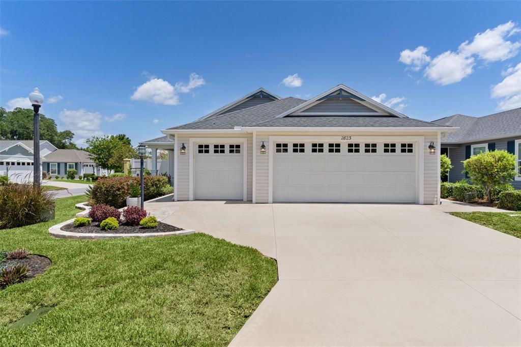 A beige house with a three-car garage and a concrete driveway under a blue sky — 2823 CHRISTOPHER COURT, THE VILLAGES, FL