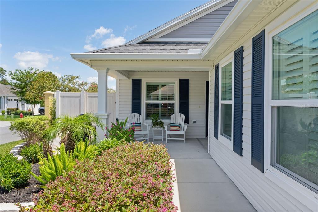 A covered front porch features white siding, dark shutters, and two white chairs — 2823 CHRISTOPHER COURT, THE VILLAGES, FL
