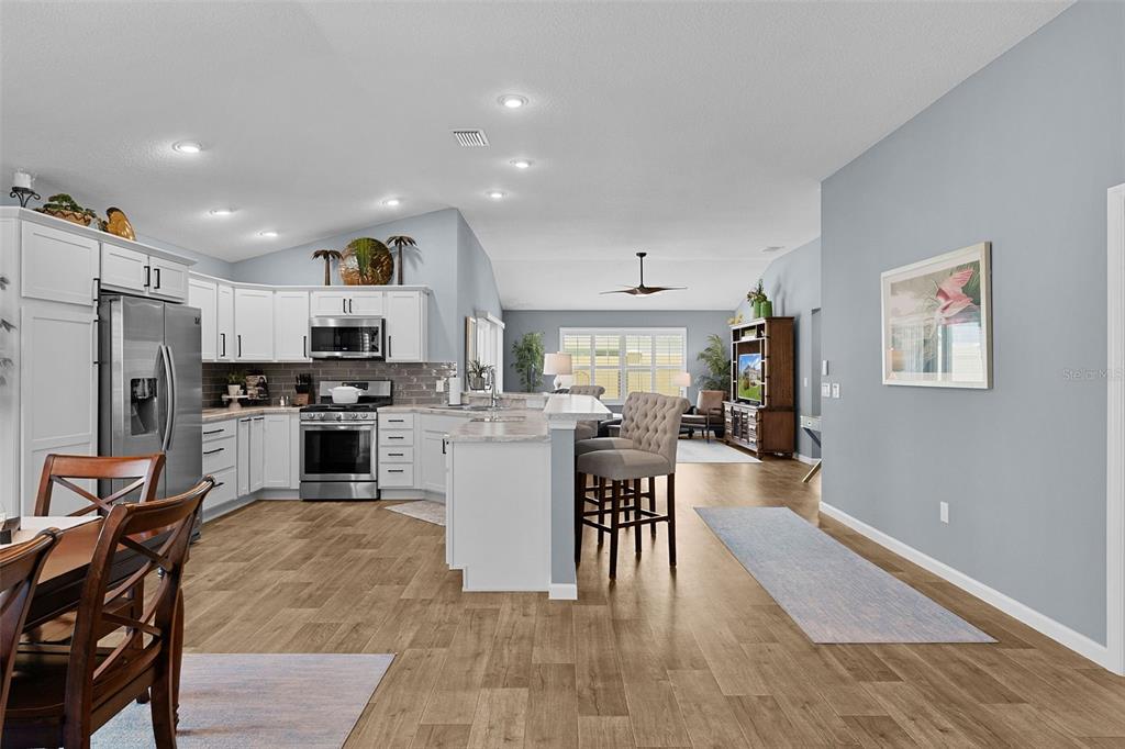 An open-concept kitchen features white cabinetry, stainless steel appliances, and a breakfast bar island — 2823 CHRISTOPHER COURT, THE VILLAGES, FL