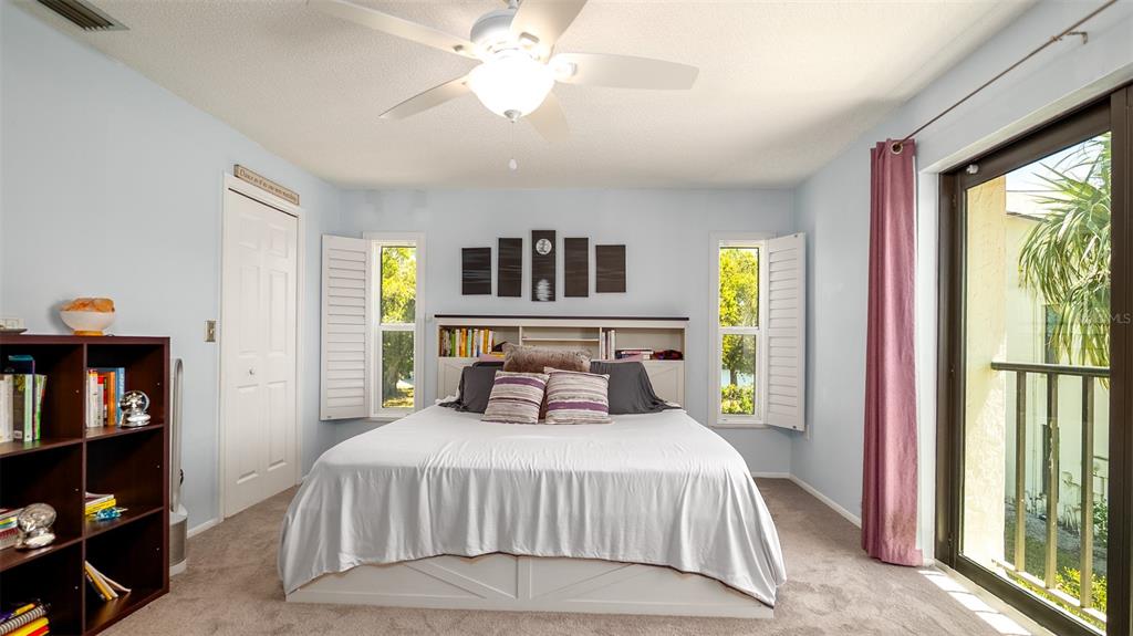 A bedroom features a bed with a headboard, a ceiling fan, and a sliding glass door — 1770 LAKE PLACE UNIT 1770D, VENICE, FL