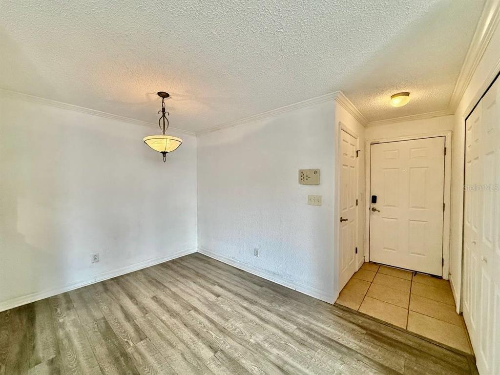 An empty dining area features wood-look flooring, a hanging light fixture, and a white front door — 3311 HAVILAND COURT UNIT 204, PALM HARBOR, FL
