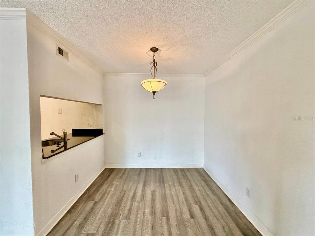 A dining area with wood-look flooring, a pendant light, and a kitchen pass-through window — 3311 HAVILAND COURT UNIT 204, PALM HARBOR, FL