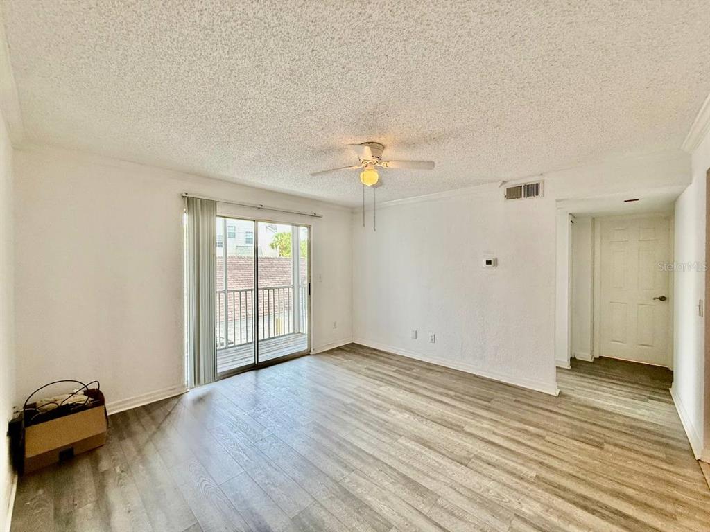 An empty living room features light wood-look flooring, a ceiling fan, and a sliding glass door — 3311 HAVILAND COURT UNIT 204, PALM HARBOR, FL