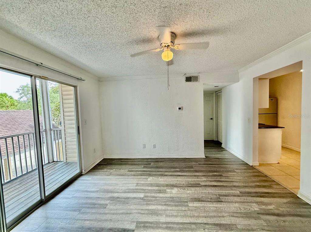 An empty living room with wood-look flooring, a ceiling fan, and a sliding glass door — 3311 HAVILAND COURT UNIT 204, PALM HARBOR, FL