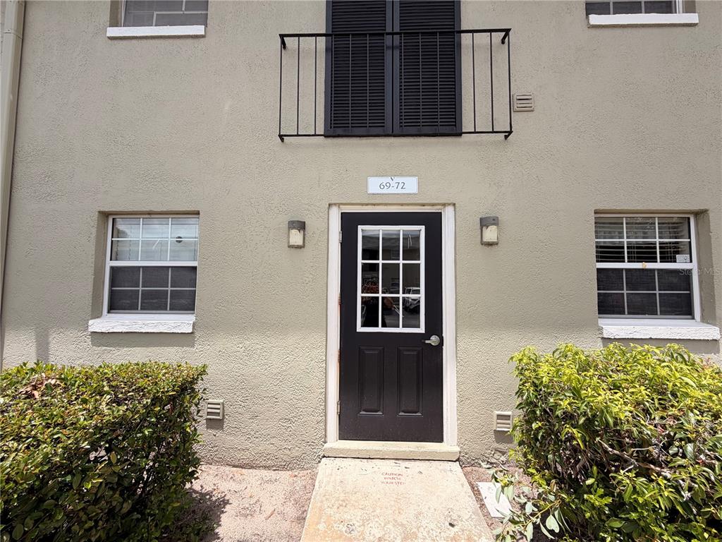 A tan stucco building exterior features a black door, a small balcony, and two windows — 525 CONWAY ROAD UNIT 72, ORLANDO, FL