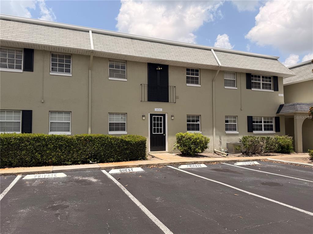 A two-story apartment building exterior features tan stucco walls, a shingled roof, and parking spaces — 525 CONWAY ROAD UNIT 72, ORLANDO, FL
