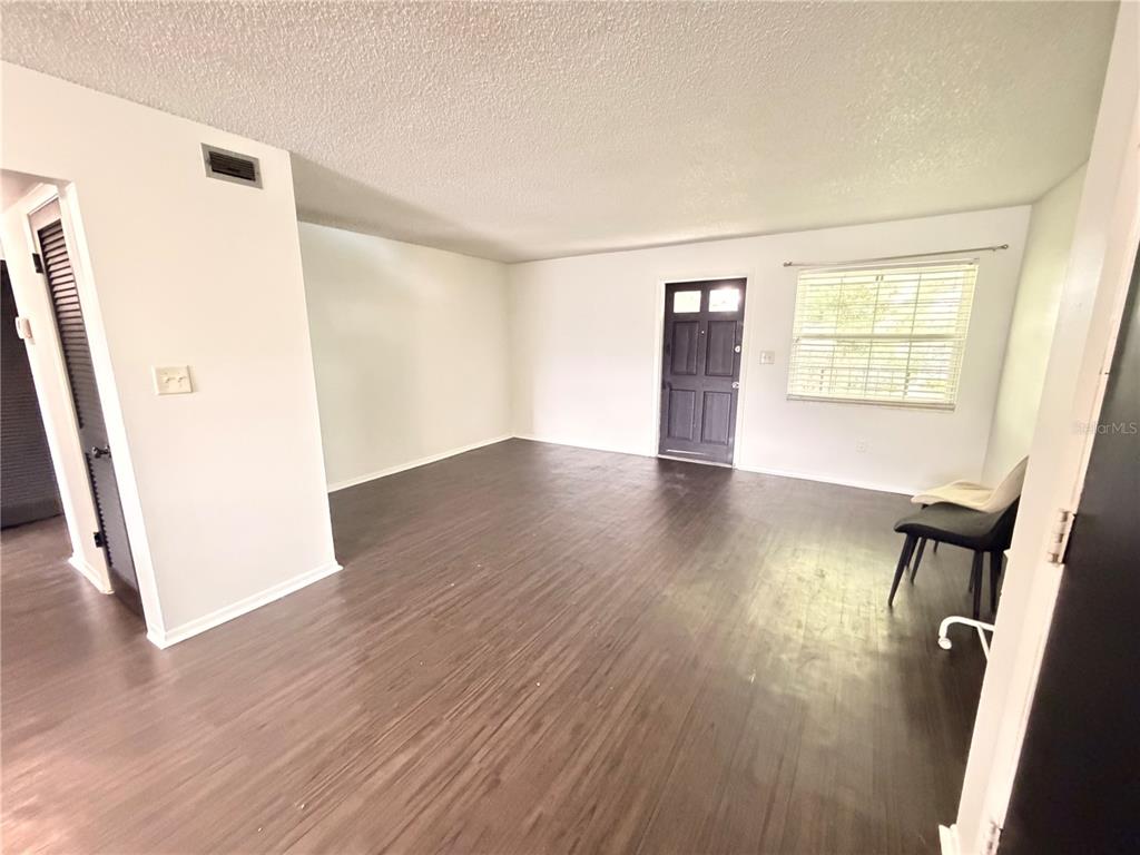 An empty living room features dark wood-look flooring, white walls, and a dark front door — 525 CONWAY ROAD UNIT 72, ORLANDO, FL