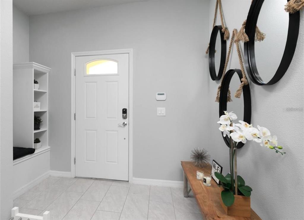 A bright entryway features a white front door, tile flooring, a wooden bench, and mirrors — 8831 GENEVE COURT, KISSIMMEE, FL