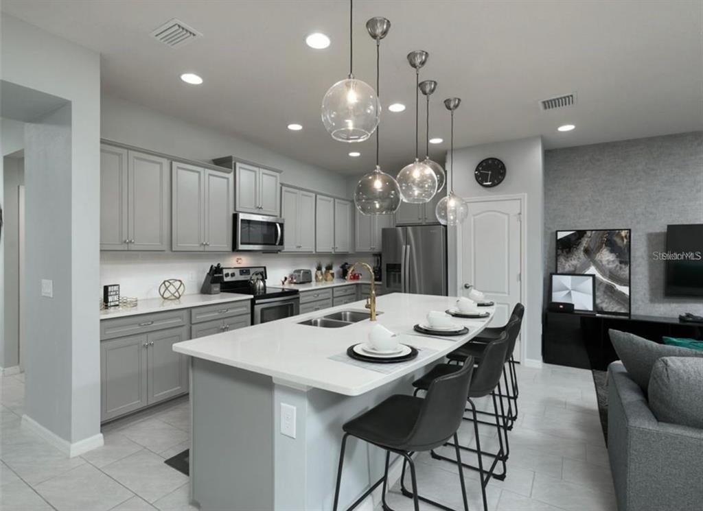 A modern kitchen features gray cabinets, a white quartz island, and glass pendant lighting — 8831 GENEVE COURT, KISSIMMEE, FL