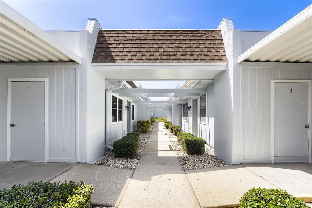 A concrete walkway leads between two rows of white exterior doors under a covered breezeway — 11210 CARRIAGE HILL DRIVE UNIT 6, PORT RICHEY, FL