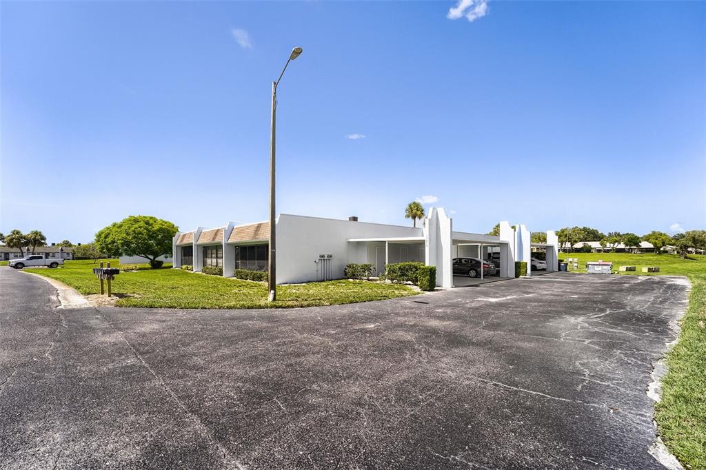 A white, single-story building features a covered carport and a large, paved parking lot — 11210 CARRIAGE HILL DRIVE UNIT 6, PORT RICHEY, FL