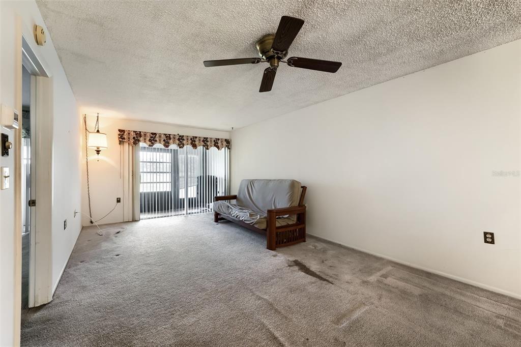 A living room features a futon, a ceiling fan, and carpeted flooring with visible stains — 11210 CARRIAGE HILL DRIVE UNIT 6, PORT RICHEY, FL