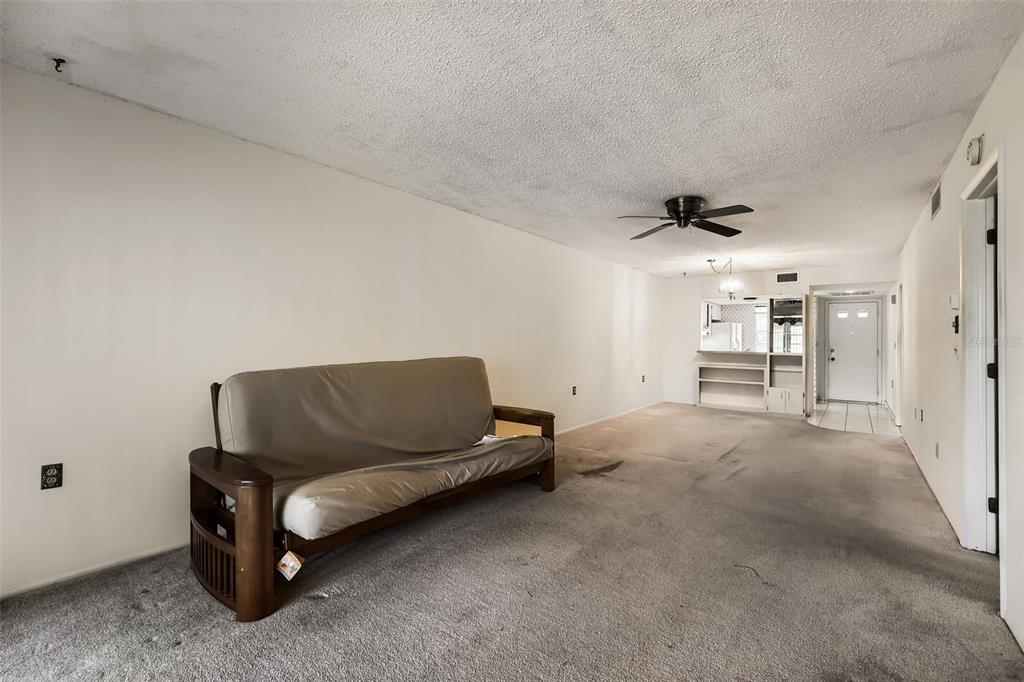 A living room features a wooden futon, gray carpeting, and a ceiling fan — 11210 CARRIAGE HILL DRIVE UNIT 6, PORT RICHEY, FL