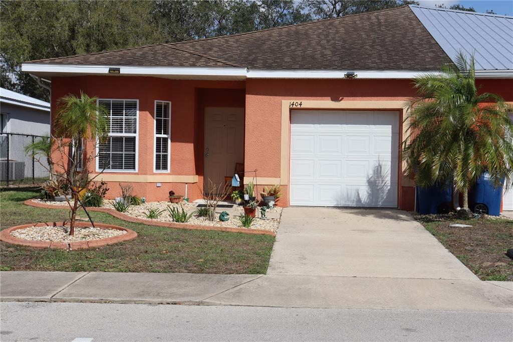 A single-story orange stucco house features a white garage door and a small front garden — 1404 LAS VILLAS BOULEVARD, SEBRING, FL