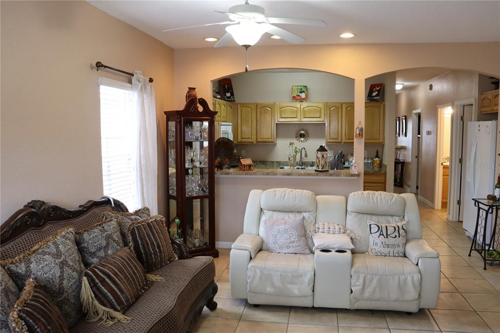 A living room with a white loveseat, a patterned sofa, and an open kitchen beyond — 1404 LAS VILLAS BOULEVARD, SEBRING, FL