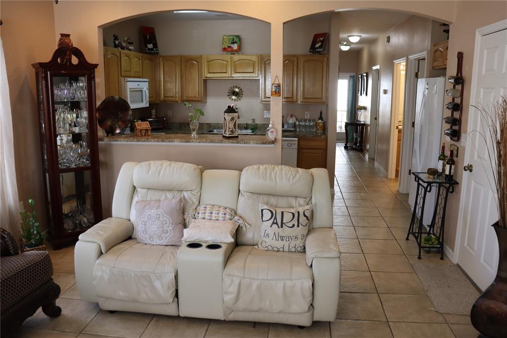 A living room with a white loveseat faces a kitchen with wood cabinets and tile flooring — 1404 LAS VILLAS BOULEVARD, SEBRING, FL