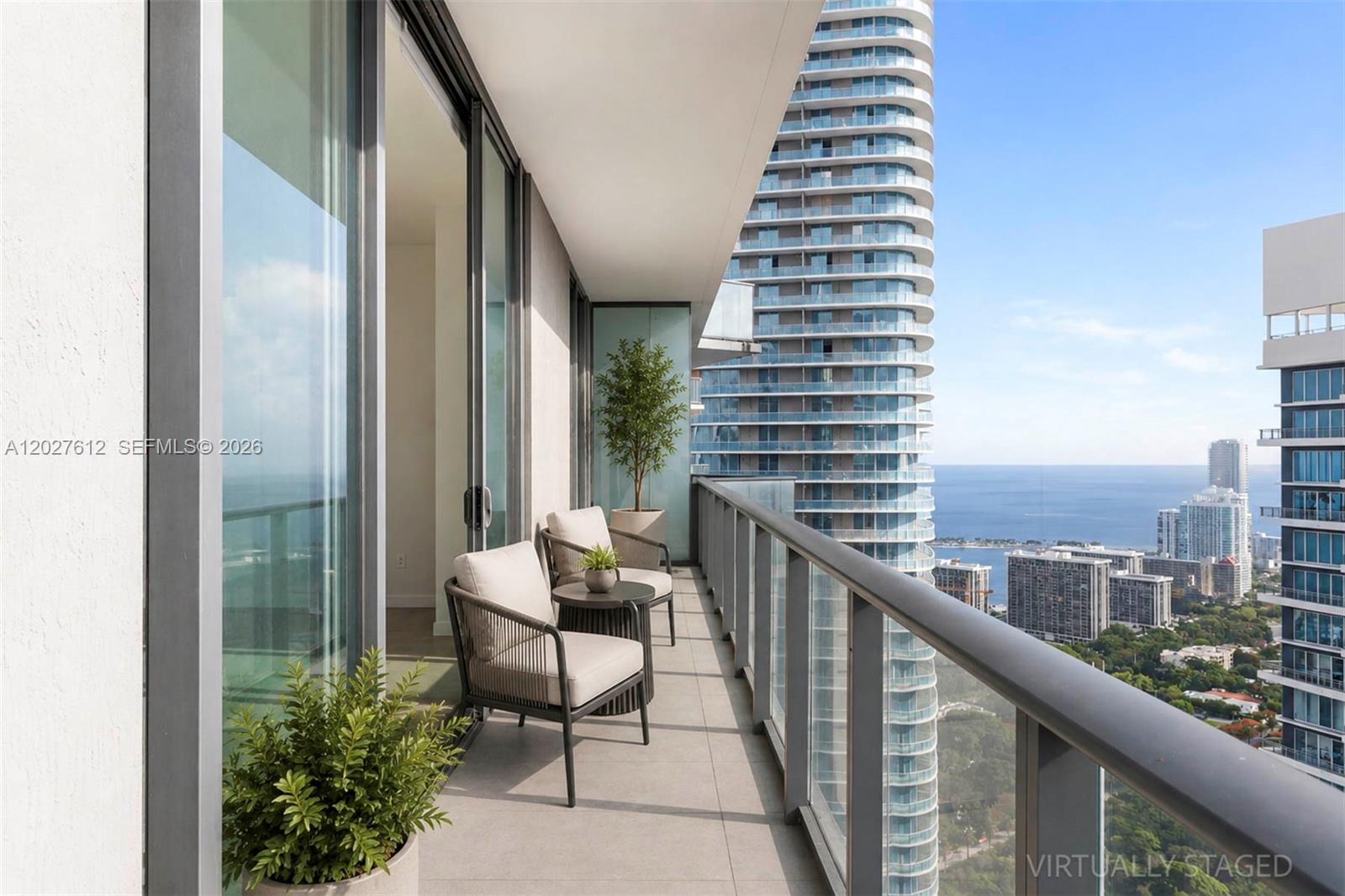 A high-rise balcony features two chairs, a small table, potted plants, and ocean views — 1300 S Miami Ave, Miami FL 33130, MIAMI, FL