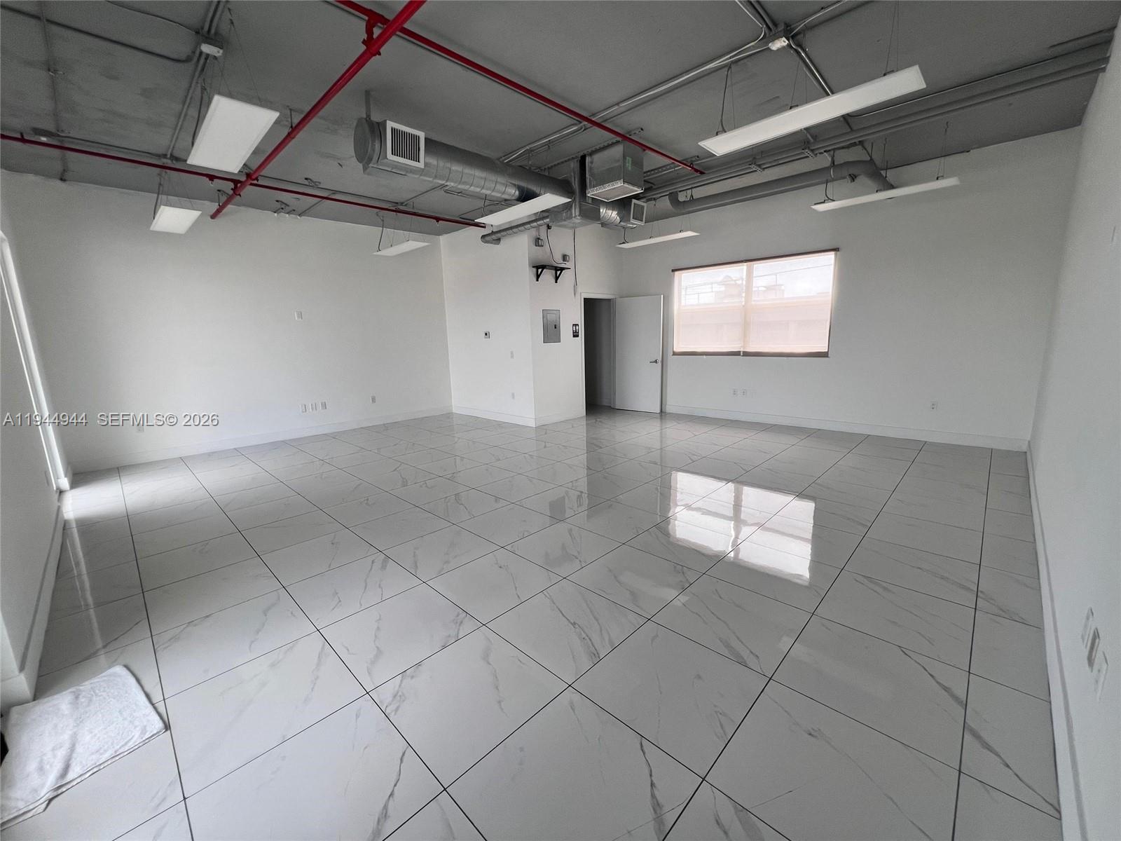 An empty office space features white marble-look tile flooring and an exposed industrial ceiling — 2721 NW 42nd Ave # 203, Miami FL 33142, MIAMI, FL