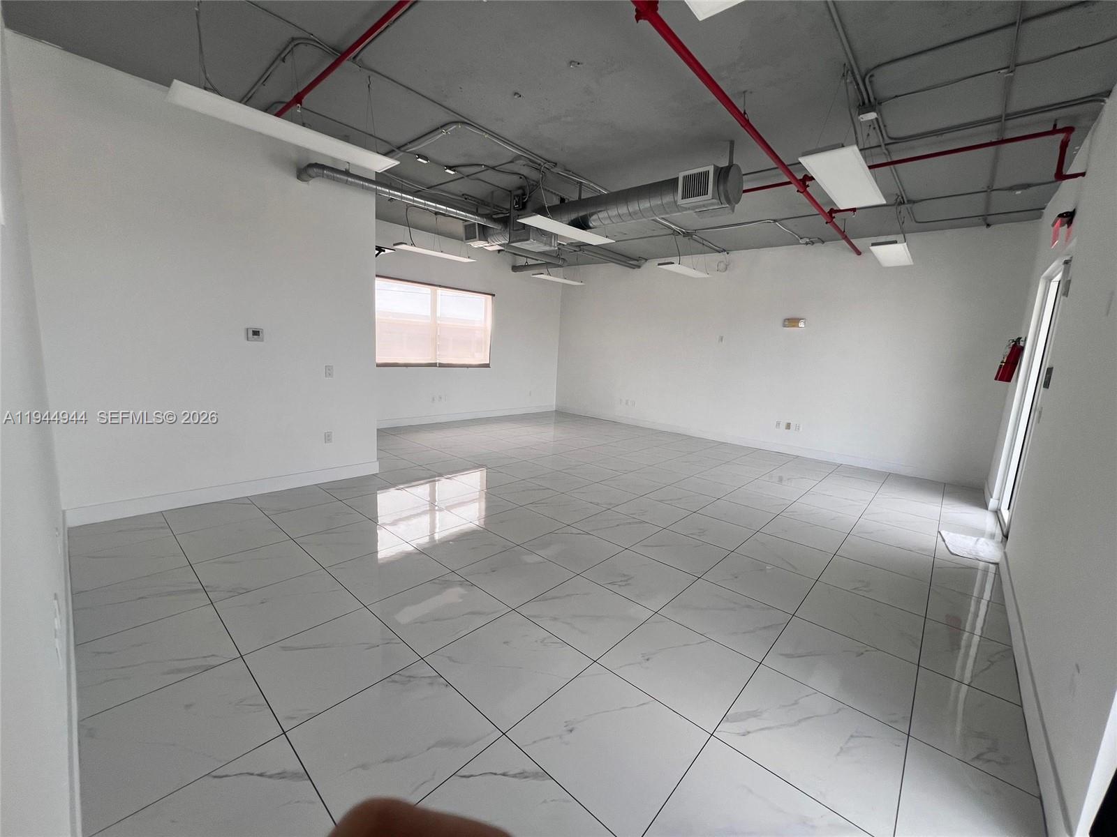 An empty commercial office space features white marble-look tile floors and an exposed industrial ceiling — 2721 NW 42nd Ave # 203, Miami FL 33142, MIAMI, FL