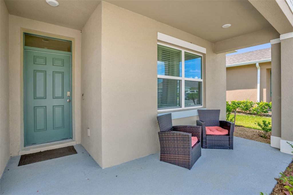 A covered front porch features a light blue door, two wicker chairs, and beige stucco walls — 5242 MAHOGANY DRIVE, MOUNT DORA, FL