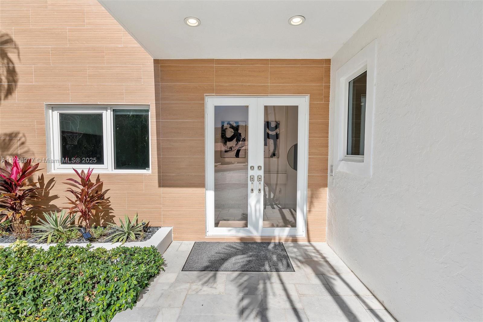 A modern home entrance features double glass doors, wood-look tile siding, and a landscaped garden — 201 Atlantic Ave, Sunny Isles Beach FL 33160, SUNNY ISLES BEACH, FL