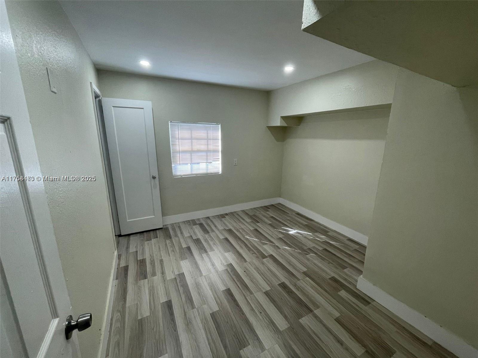 An empty room features light-colored walls, wood-look laminate flooring, a single window, and a white door — 4896 SW 28th Ter, Dania Beach FL 33312, DANIA BEACH, FL