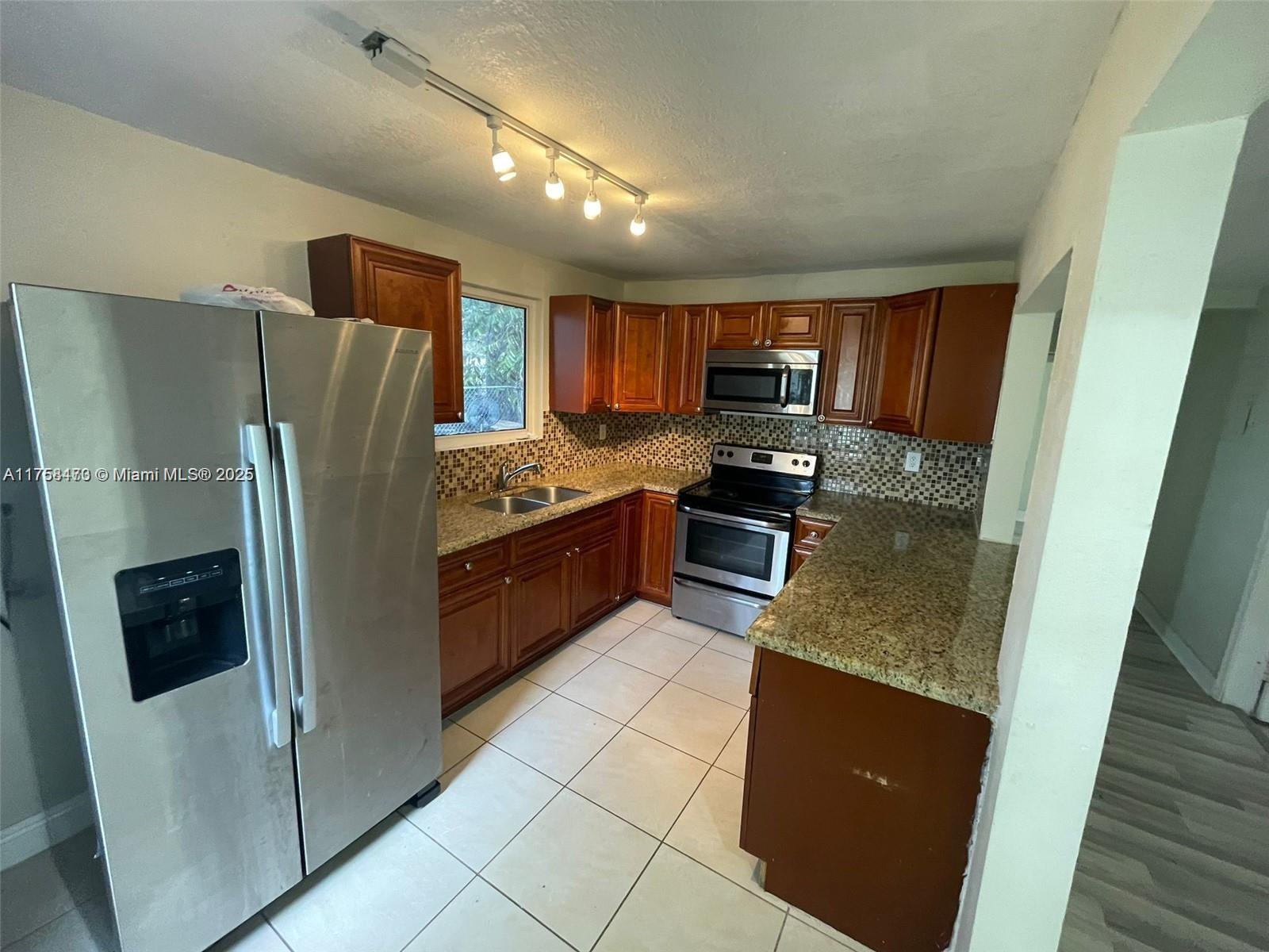 A kitchen features wood cabinets, granite countertops, stainless steel appliances, and light-colored tile flooring — 4896 SW 28th Ter, Dania Beach FL 33312, DANIA BEACH, FL